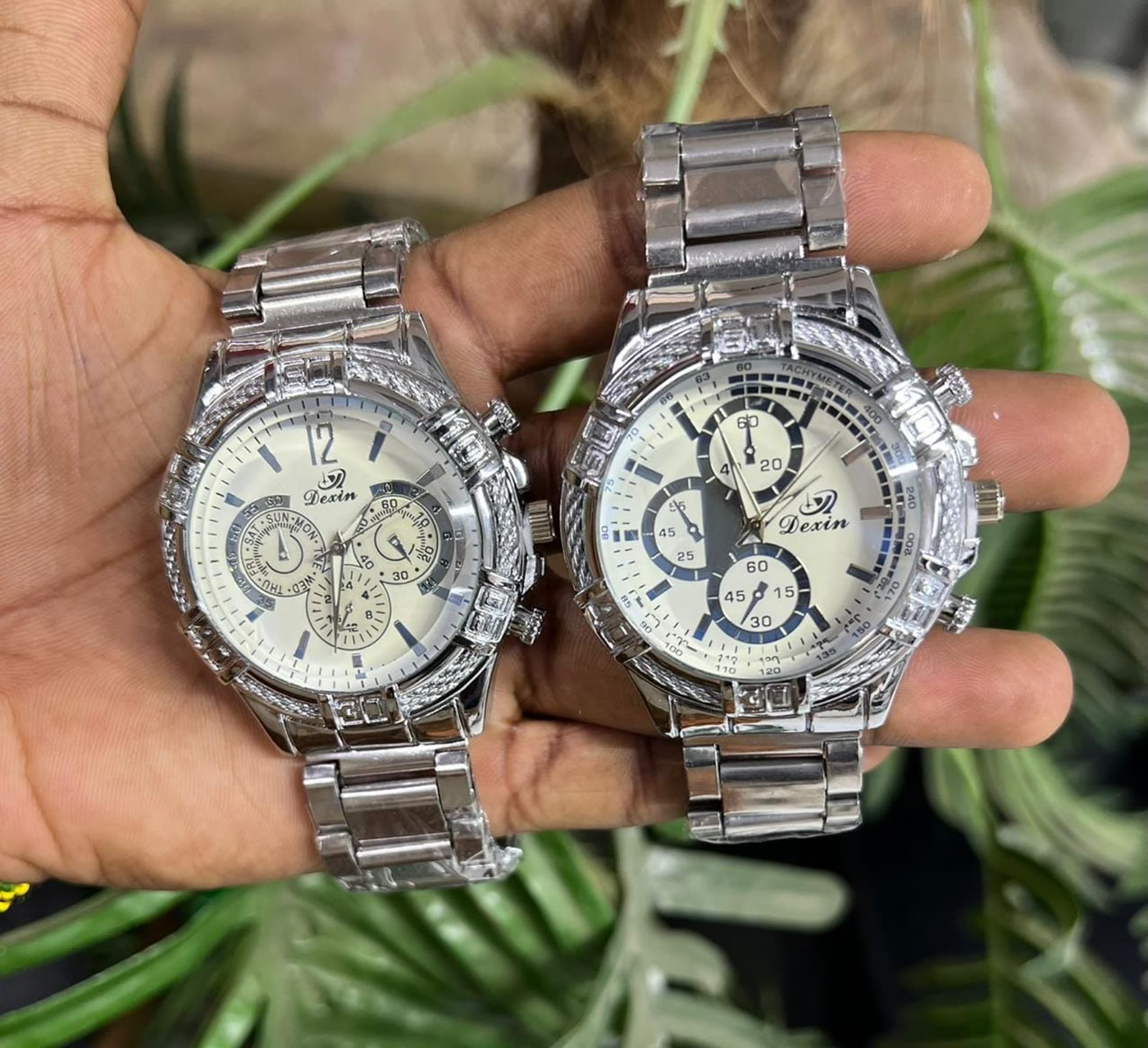 Two stone-set steel watches held up in the shop