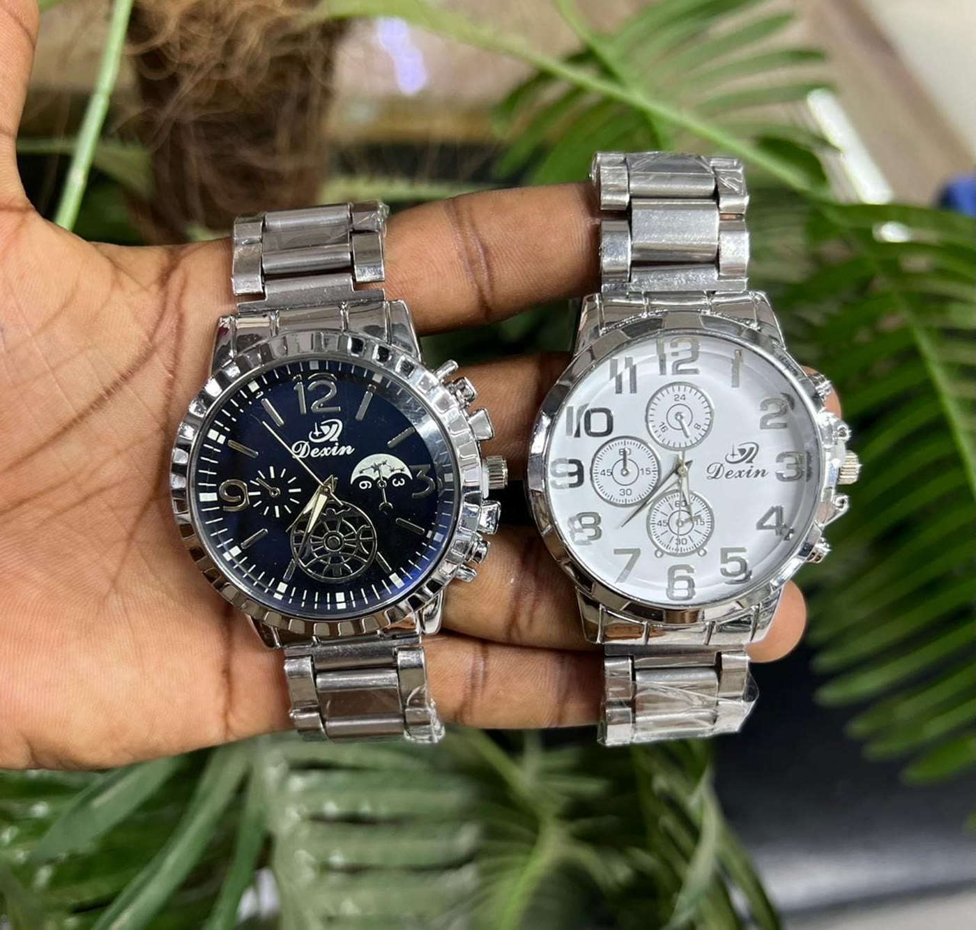 Two steel chronograph watches held in a hand in the shop
